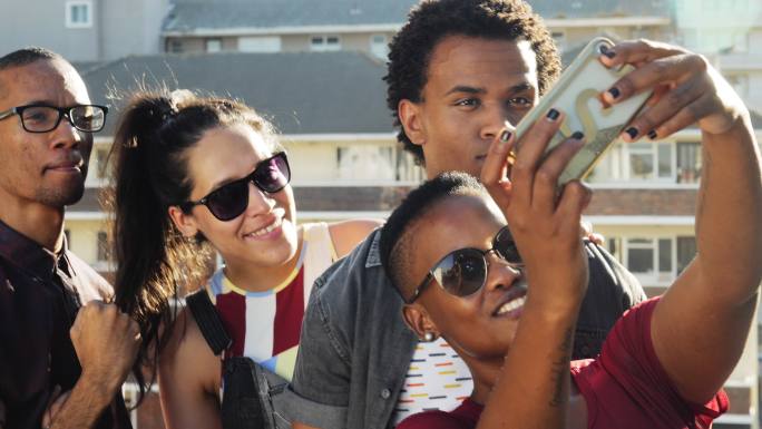 年轻朋友在阳光明媚的城市露台上用智能手机自拍
