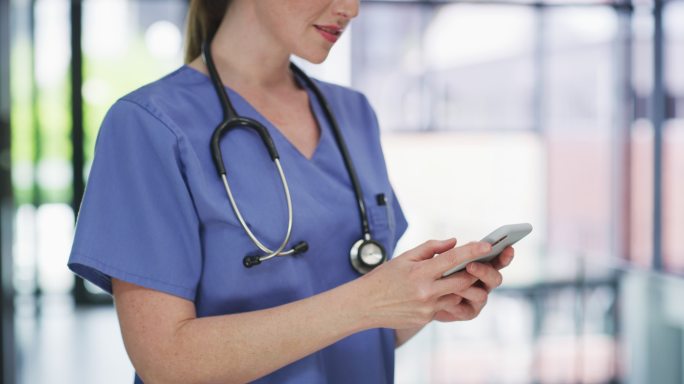 一个无法辨认的护士独自站在诊所里使用手机的4k视频片段
