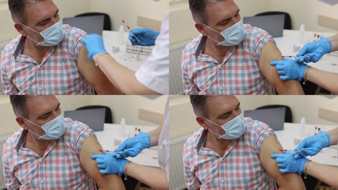 一名成年男子坐在医生办公室，由女医务工作者接种新冠疫苗