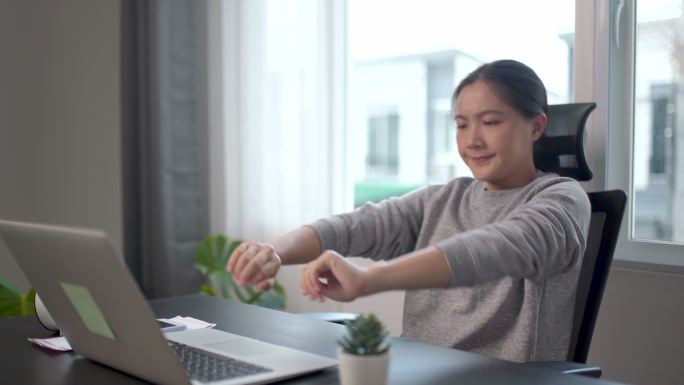 一名在家庭办公室用笔记本电脑工作的亚洲妇女身体疼痛。