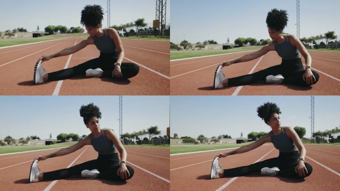 在跑道上跑步和在运动中心或体育场训练之前，在热身中有非洲伸展腿的运动员。专注，严肃，健康，运动女性坐