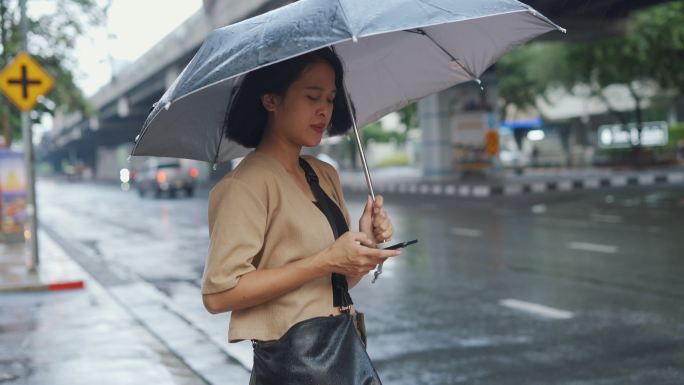 一名亚洲妇女在雨中等出租车时使用手机