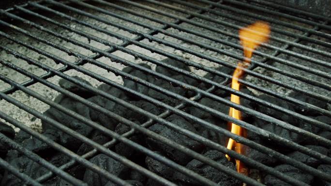 一个高加索人的手把点燃的木柴扔到户外烧烤架上，点燃木炭块准备烧烤