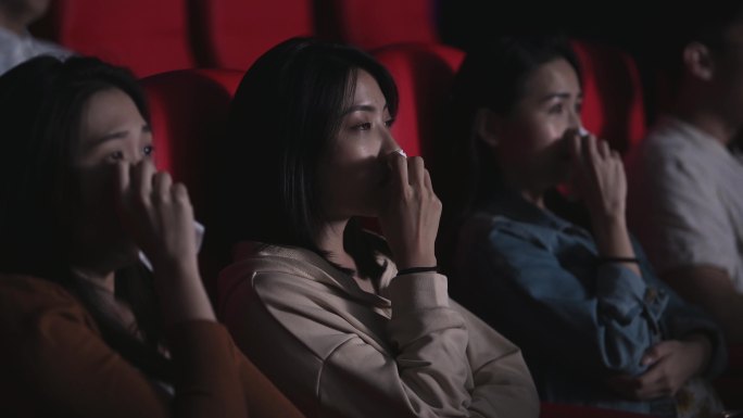 亚裔中国妇女在电影院里哭泣，观看伤感的戏剧电影。电影院，用纸巾擦眼泪
