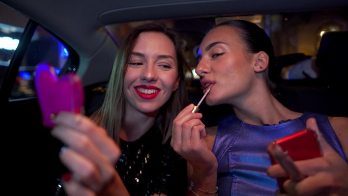 快乐的年轻女性在汽车后座上准备派对，正在化妆