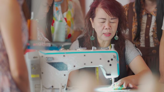 亚洲华裔高级女裁缝师，在工作室车间展示她的学生在缝纫课上