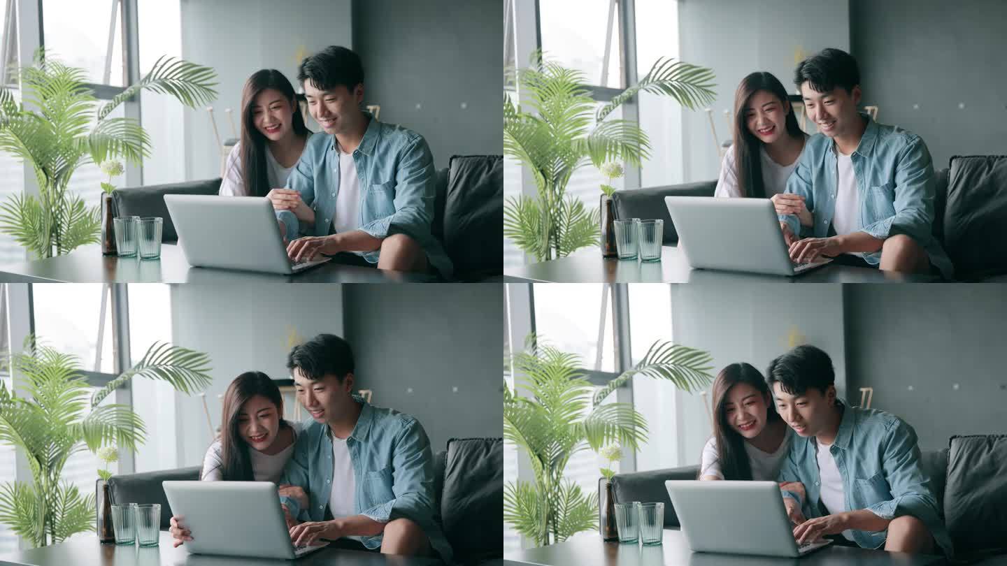 一对年轻夫妇坐在家里的沙发上使用笔记本电脑