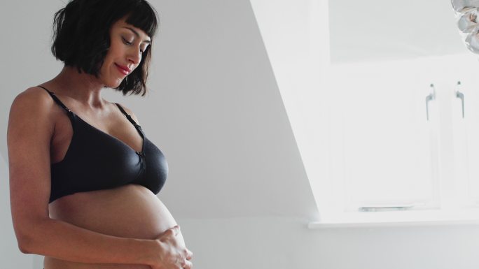 穿着胸罩和内裤的孕妇在育婴室触摸胃部