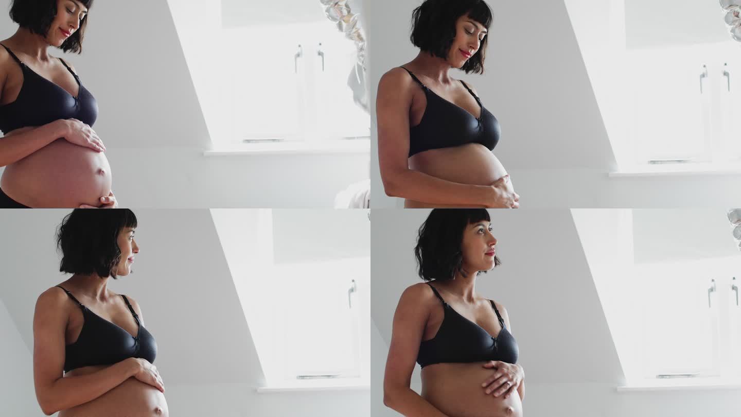 穿着胸罩和内裤的孕妇在育婴室触摸胃部