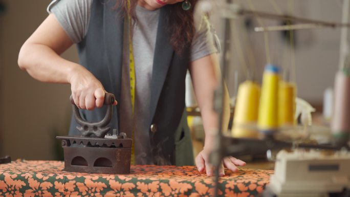 特写：一位亚洲华裔高级女性裁缝在她的工作室里手工使用传统的古董熨斗器具熨烫布料