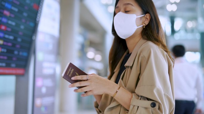 一个女商人戴着口罩在数字时刻表上检查登机时间。