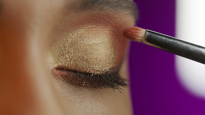 一个女孩的眼睛特写，化妆师用化妆刷涂眼影。