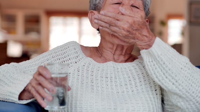一位亚洲老年妇女感到不舒服，在家里吃药片或服用维生素。医疗、护理、退休、生活方式、医疗保健和医学、老