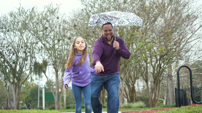 西班牙女孩和父亲在雨中伞下奔跑