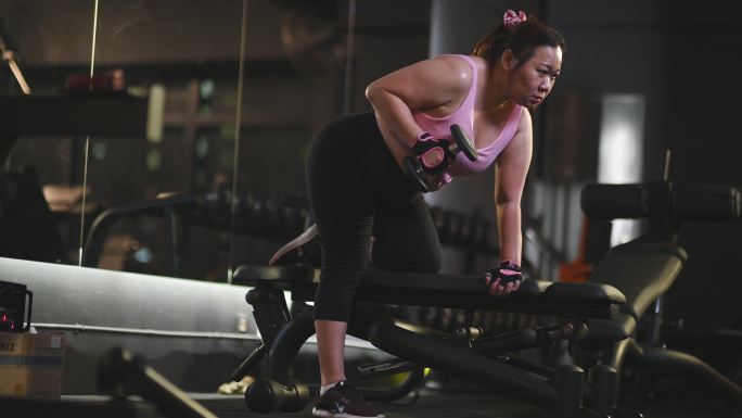 身体积极的亚洲中年女性，晚上在健身房以弓箭步姿势练习哑铃