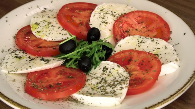 卡普里斯沙拉配成熟的西红柿和马苏里拉奶酪，新鲜的罗勒叶放在餐桌背景上。塞尔维亚食品库存视频