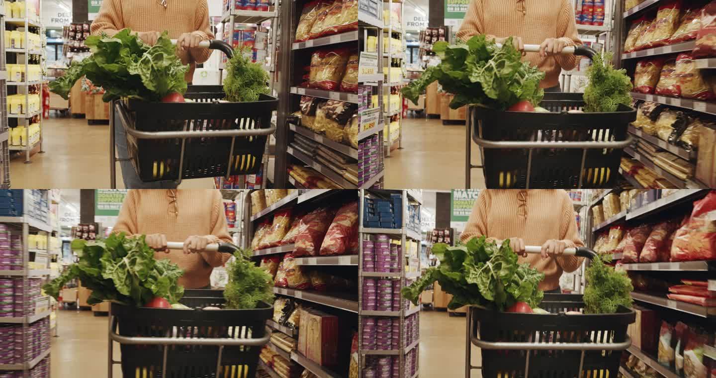 一名女顾客在超市里推着一辆装有蔬菜的手推车。一位健康的纯素女性手拿购物车，在当地商店货架上寻找新鲜农