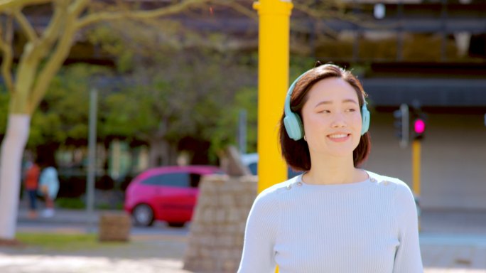 一个美丽的年轻女子戴着耳机在城市散步时喝咖啡的4k视频片段