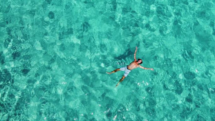 一名男子在美丽透明的绿松石海中放松的鸟瞰图