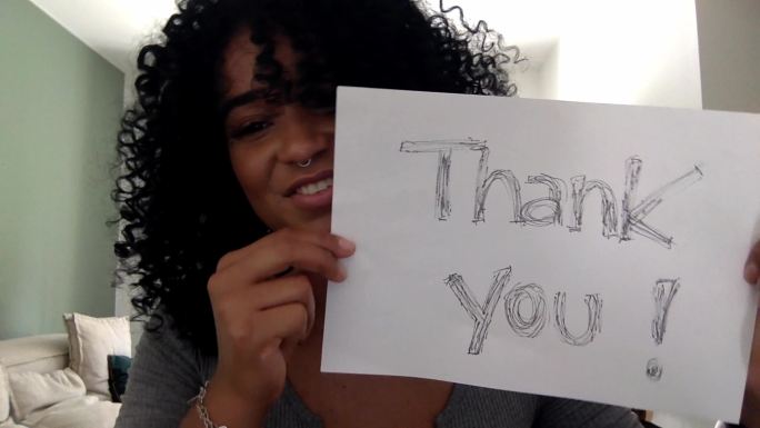 年轻女子拿着写在家里的“谢谢”的纸-网络摄像头的观点