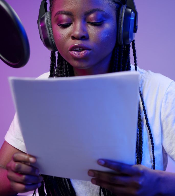 在紫色背景的演播室里，一位年轻的黑皮肤电台dj穿着白色t恤，扎着长长的辫子，对着专业麦克风读着报纸上