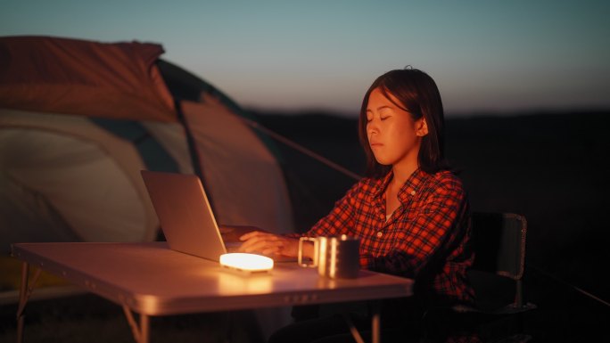 在大自然露营时，一名年轻女子在帐篷旁使用笔记本电脑