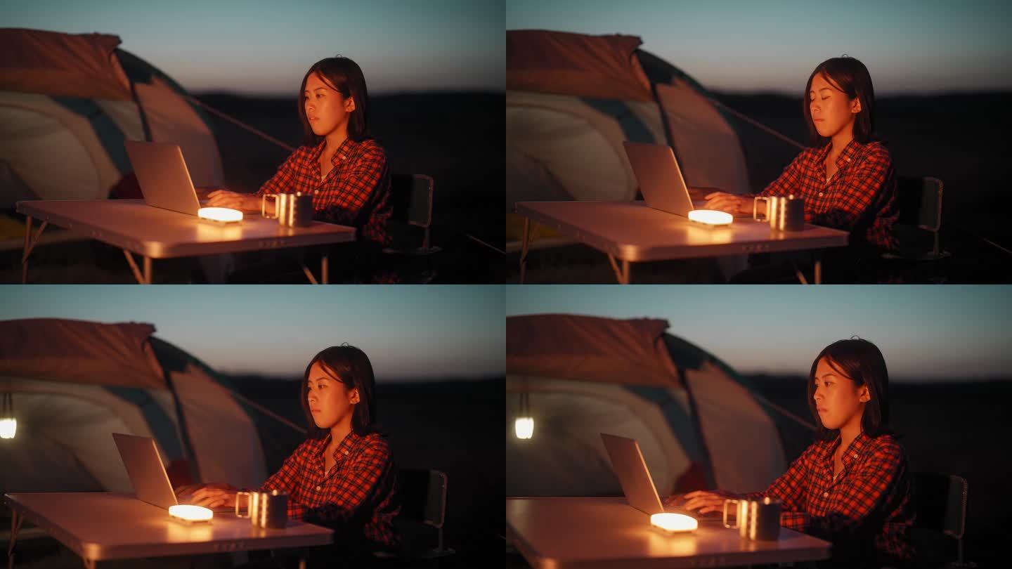 在大自然露营时，一名年轻女子在帐篷旁使用笔记本电脑