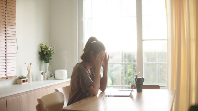 一名亚洲妇女在家里使用笔记本电脑时遇到了麻烦。