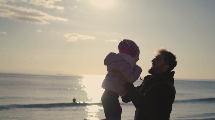 父亲把女儿扔到空中，超慢动作，父亲在冬天的海滩上把女儿扔在空中
