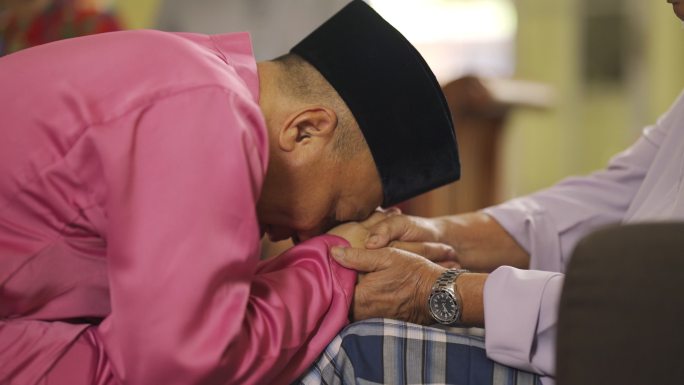 斋月：马来穆斯林的儿子穿着传统服装，在艾迪尔菲里庆典上向父亲表示道歉。马来家庭在家里庆祝开斋节