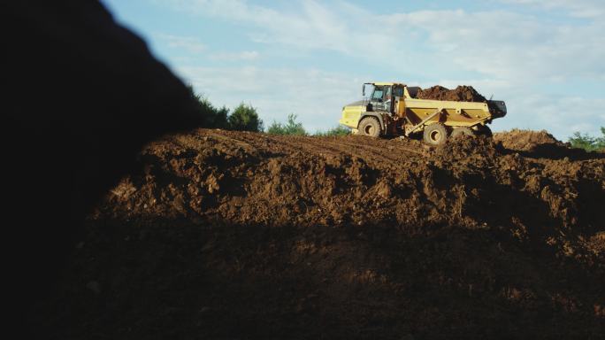 在一个阳光明媚的日子里，一辆自卸卡车满载着泥土在一个新建筑工地的山坡上倒车