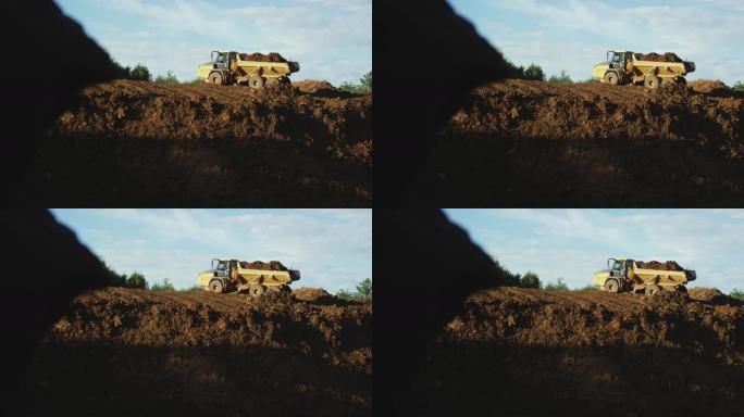 在一个阳光明媚的日子里，一辆自卸卡车满载着泥土在一个新建筑工地的山坡上倒车