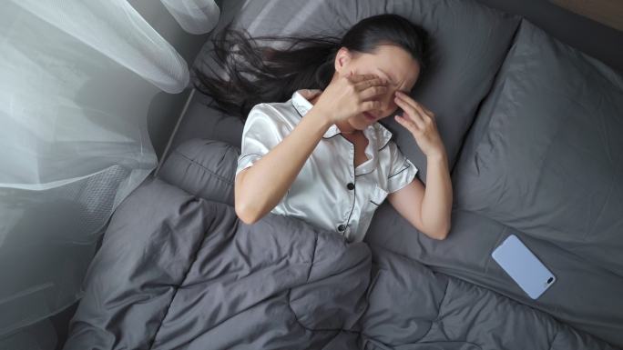 一名亚洲妇女早上躺在床上，眼睛疼痛。俯视图。