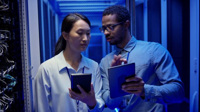 男性和女性网络工程师在服务器室使用平板电脑进行故障排除，并检查服务器