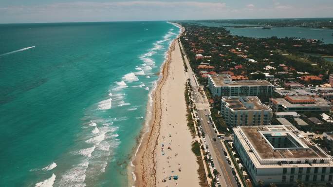 2021 5月新冠肺炎期间的中午，佛罗里达棕榈滩充满活力的青色海洋海岸鸟瞰图，海滩上挂满了彩色的沙滩