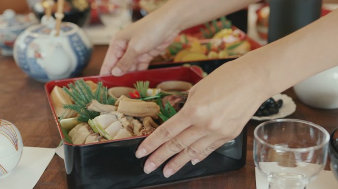 特写-女性手将传统的日本Osechi放在餐桌上。