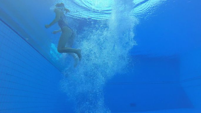 SLO-MO-LD水下视图：一名女跳水运动员降落在游泳池中，在一团气泡中旋转