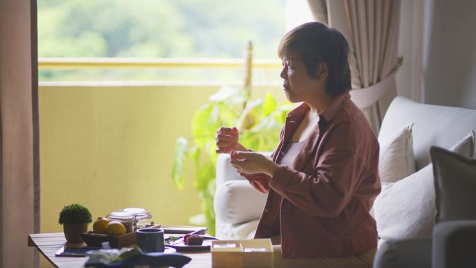 一名亚裔中国妇女在客厅切雪皮月饼，享用下午茶和中国传统节日甜点