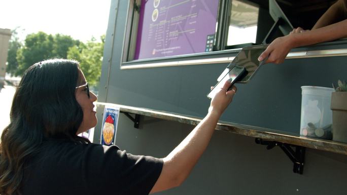 一名年轻女子手持智能手机，在食品卡车租售点扫描NFC移动无现金支付