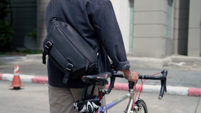 年轻的亚洲送货员推着自行车穿过街道。