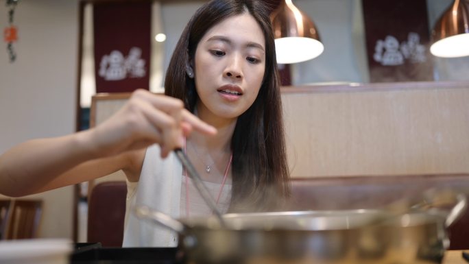 Genration Z微笑的亚洲女性正在吃涮涮锅或Sukiyaki，这是一道受欢迎的猪肉、牛肉、虾、