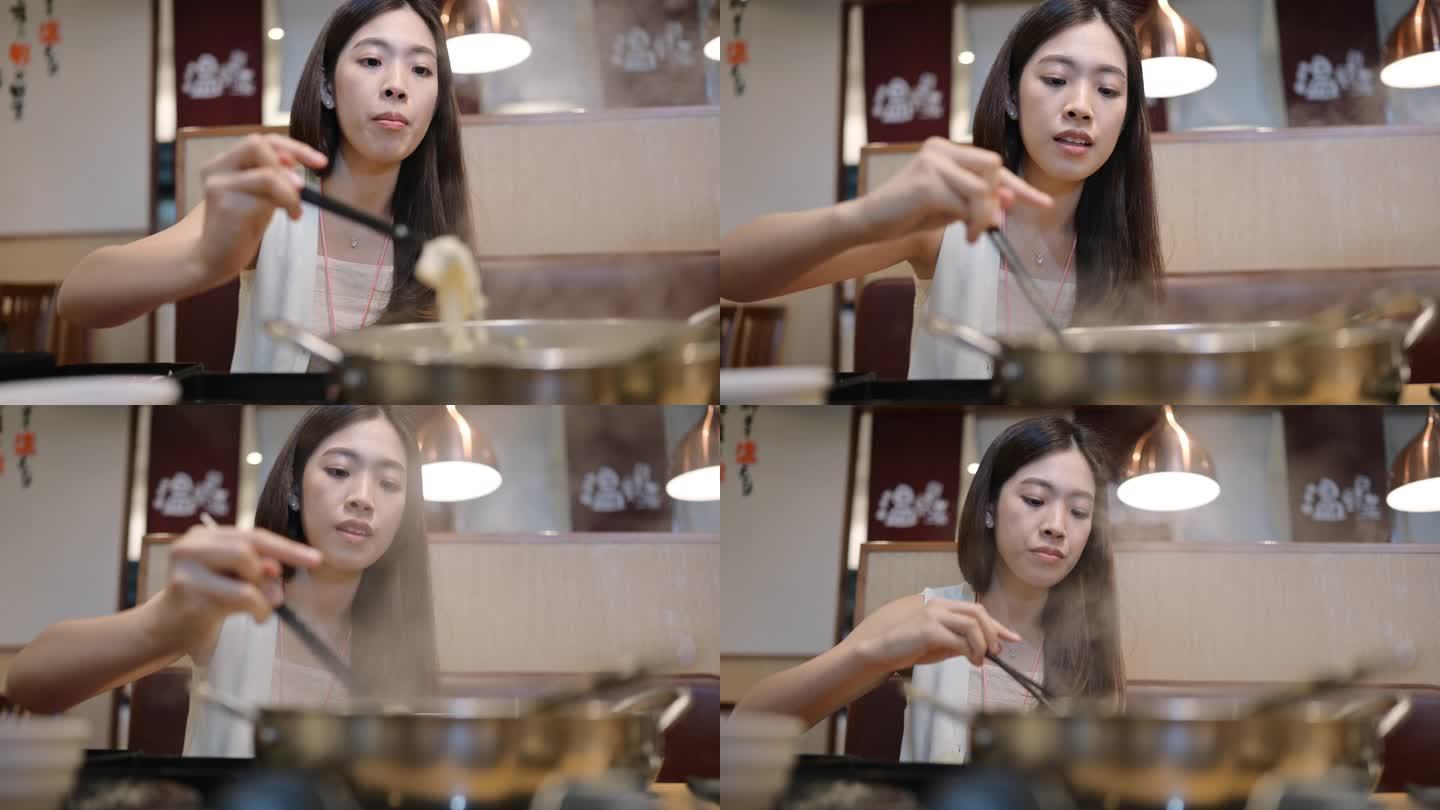 Genration Z微笑的亚洲女性正在吃涮涮锅或Sukiyaki，这是一道受欢迎的猪肉、牛肉、虾、