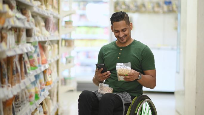 周末，一名残疾亚裔印度男子坐轮椅在超市购物，用他的智能手机查看购物清单