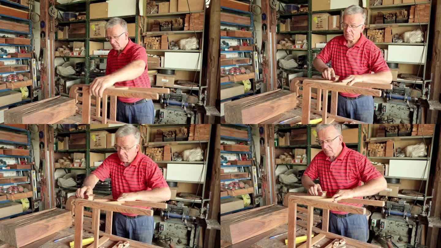 一位老人正在木工车间的长凳上打磨椅子