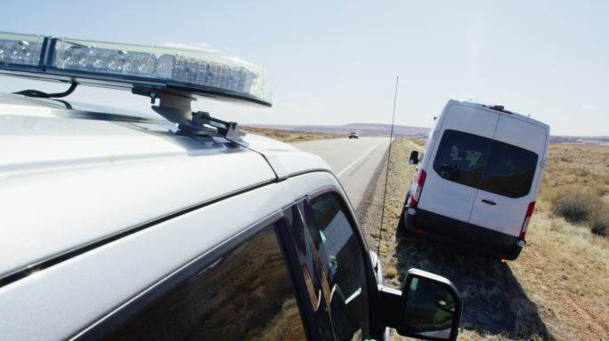 在一个阳光明媚的日子里，一辆警车在犹他州沙漠中的高速公路/州际公路旁驶过一辆白色大面包车