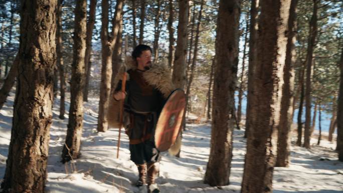 中世纪中年武士，在日落时手持长矛和盾牌穿过森林