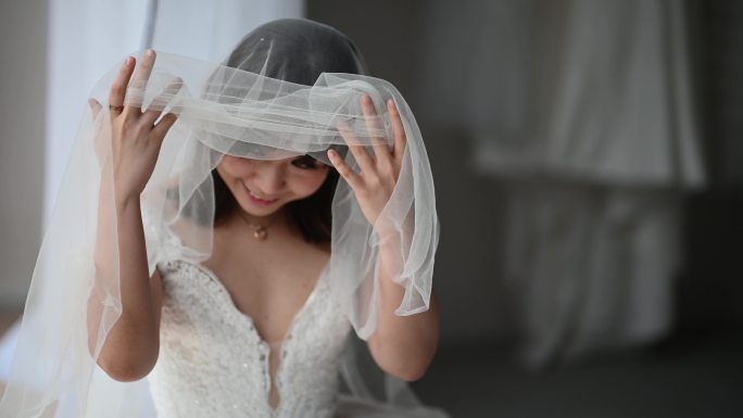 美丽的亚洲中国新娘拉上面纱，偷看，等待她的新郎在婚礼当天微笑