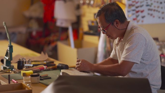 一位亚裔中国高级男子在他的工作室里制作手工皮革表带