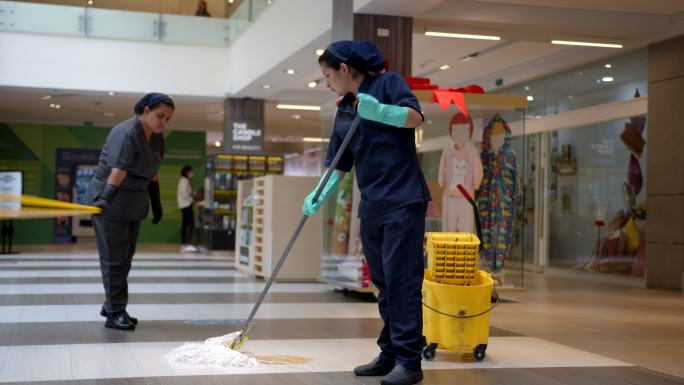 商场里的女清洁工在晾干时为湿滑的地板贴上警告标志