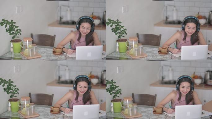 亚裔中国美女微笑着参加在线课堂，在厨房使用笔记本电脑进行视频通话